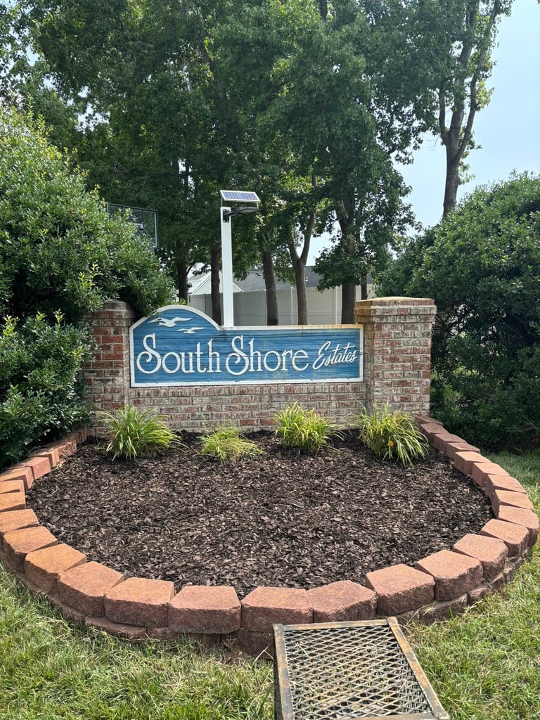 South Shore Estates community sign with blue lettering on brick base surrounded by decorative plants and landscaping